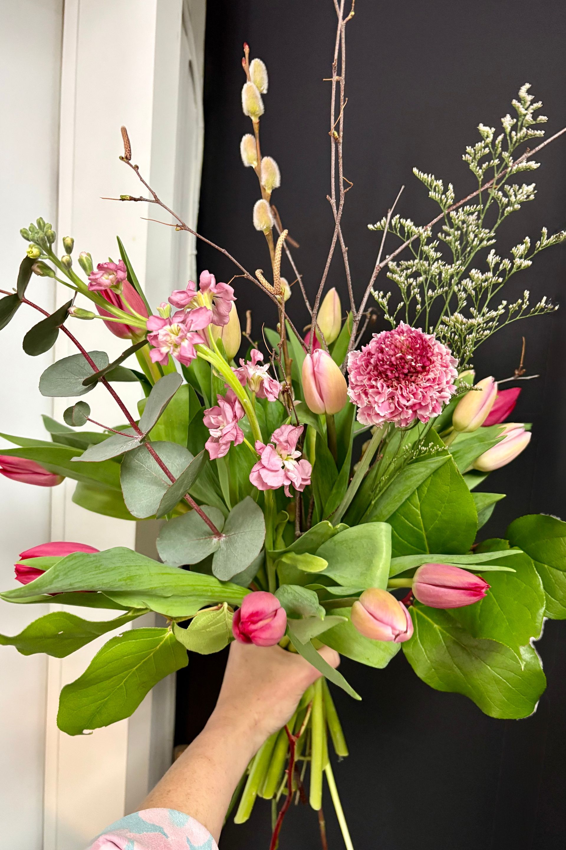 Bouquet de tulipes roses, de roses et de verdure tenu à la main sur fond sombre