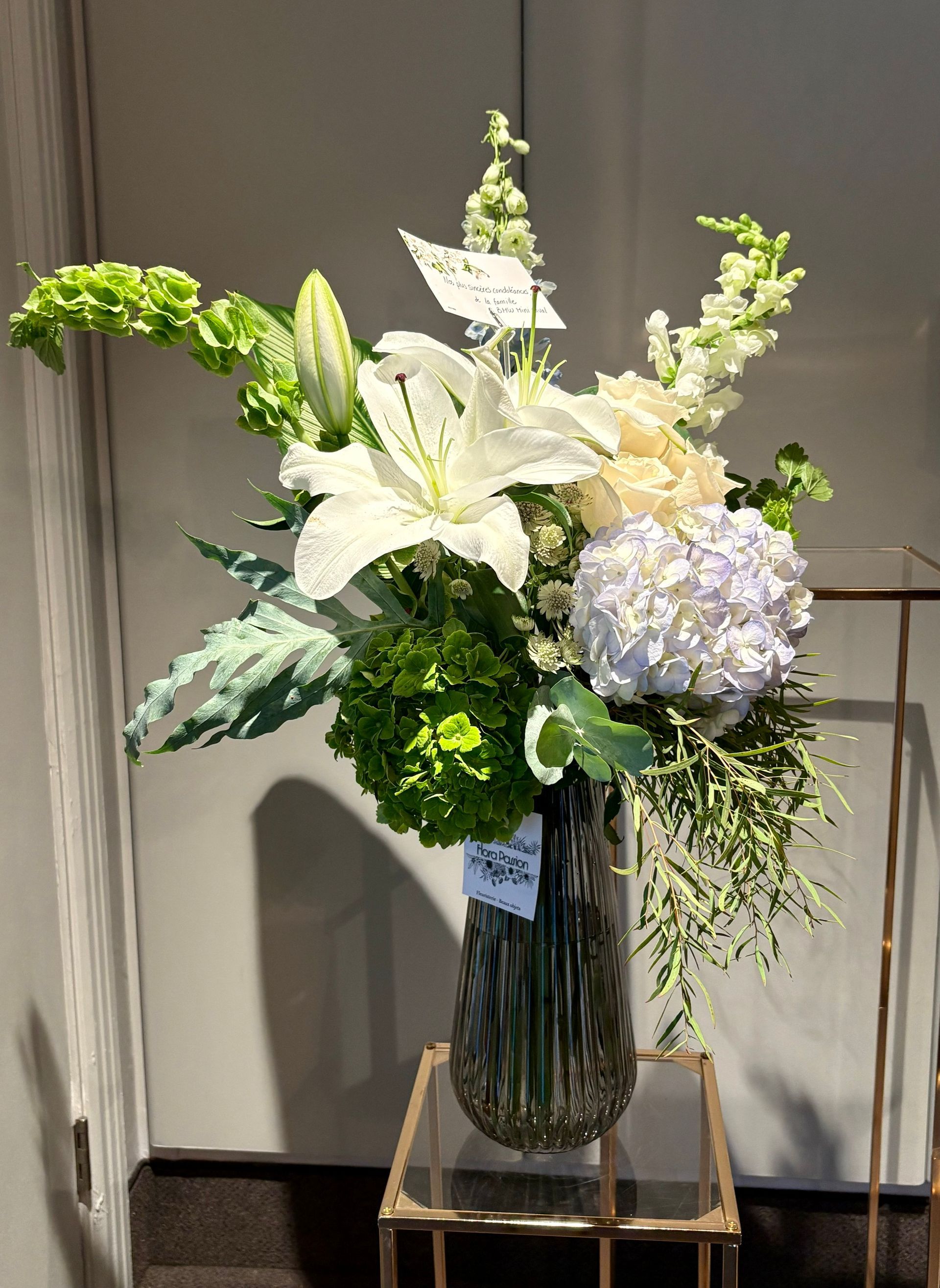 Composition florale blanche et bleu pâle dans un grand vase en verre sur une petite table