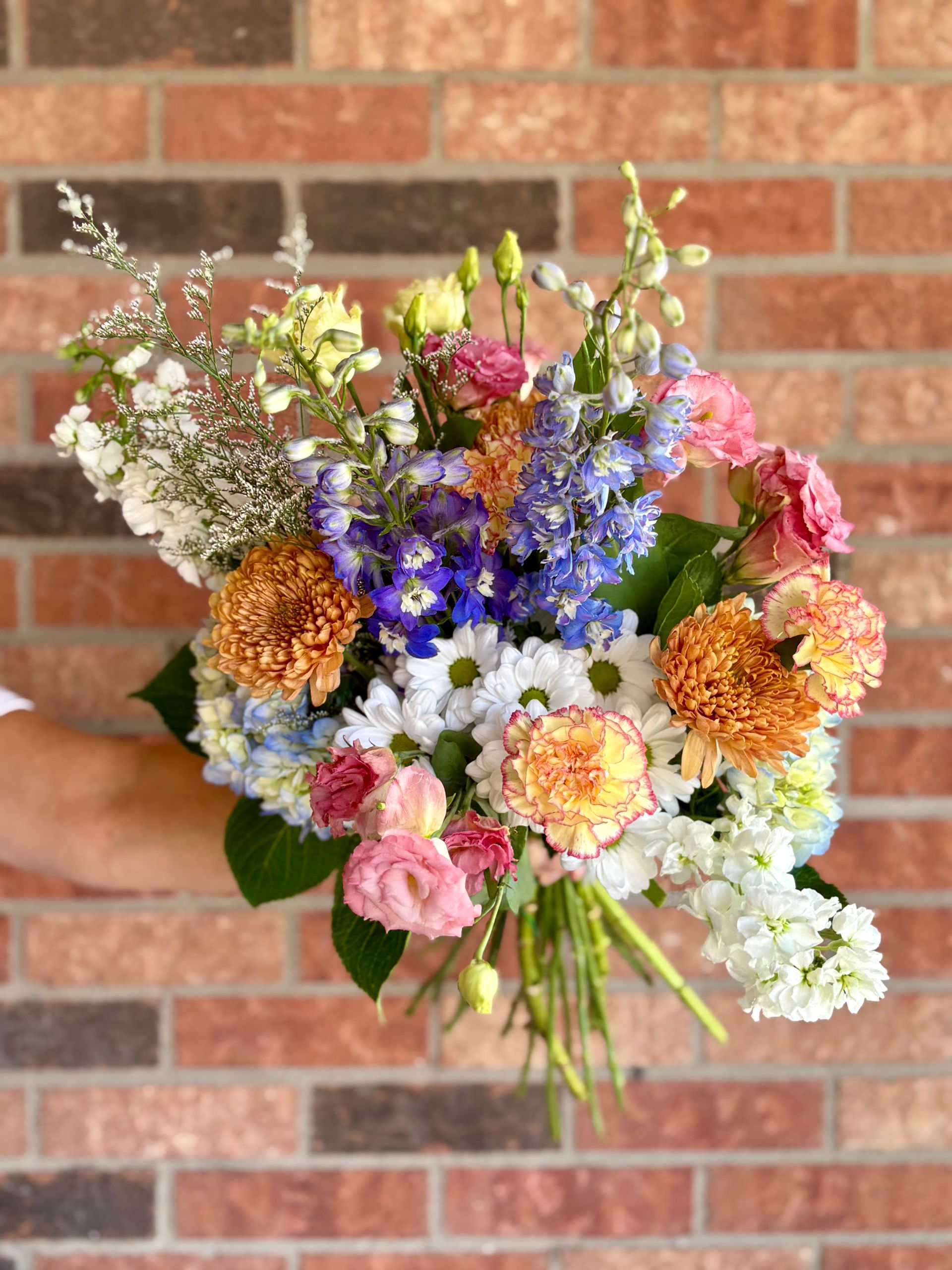 Bouquet de fleurs colorées porté à la main devant un mur de briques