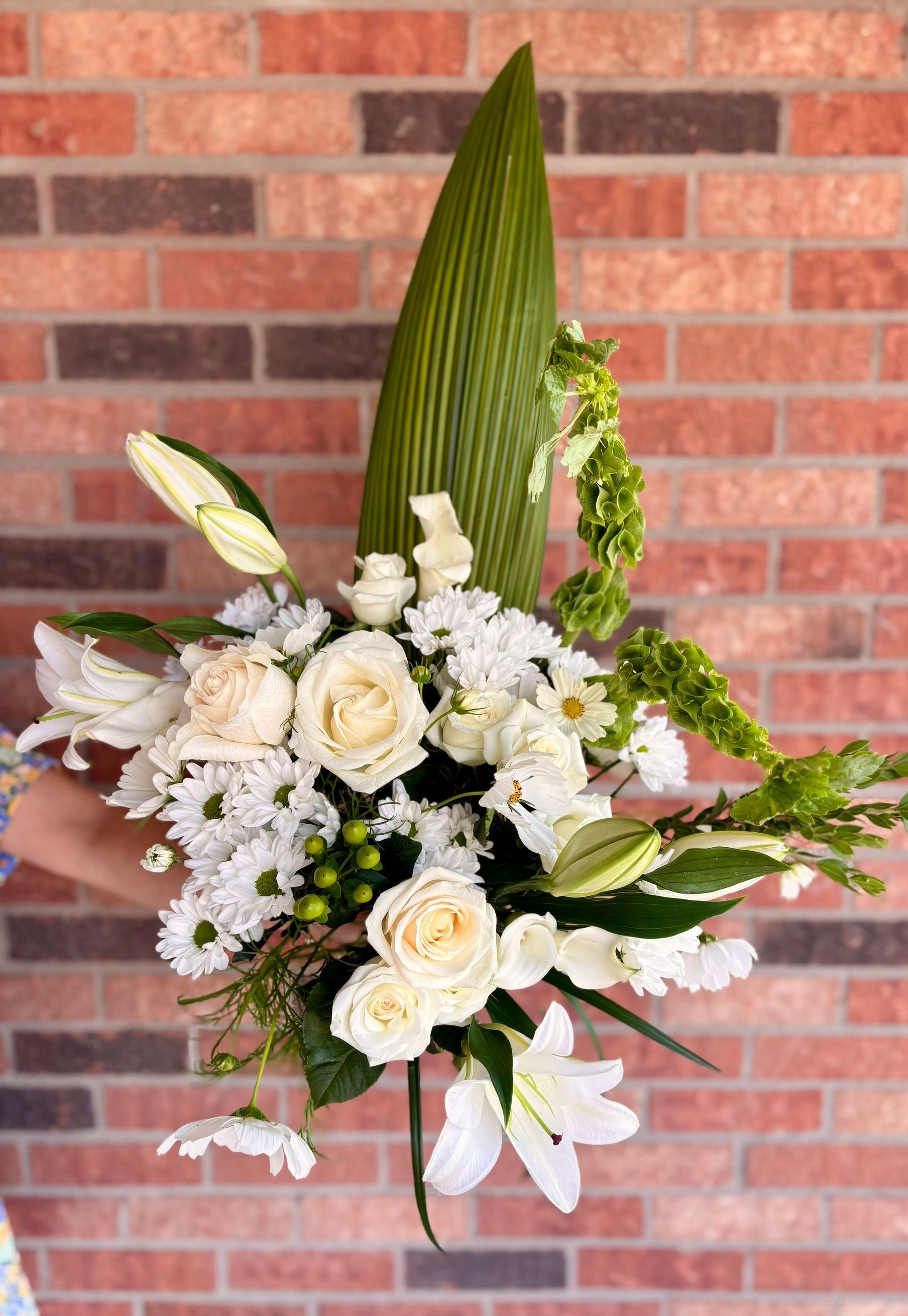 Composition florale blanche et crème avec des lys et des roses devant un mur de briques