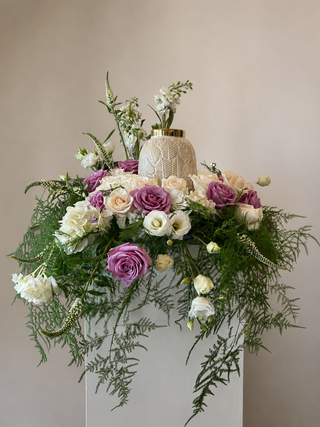 Gâteau de mariage blanc orné de fleurs roses et blanches et de feuillage retombant sur un fond beige