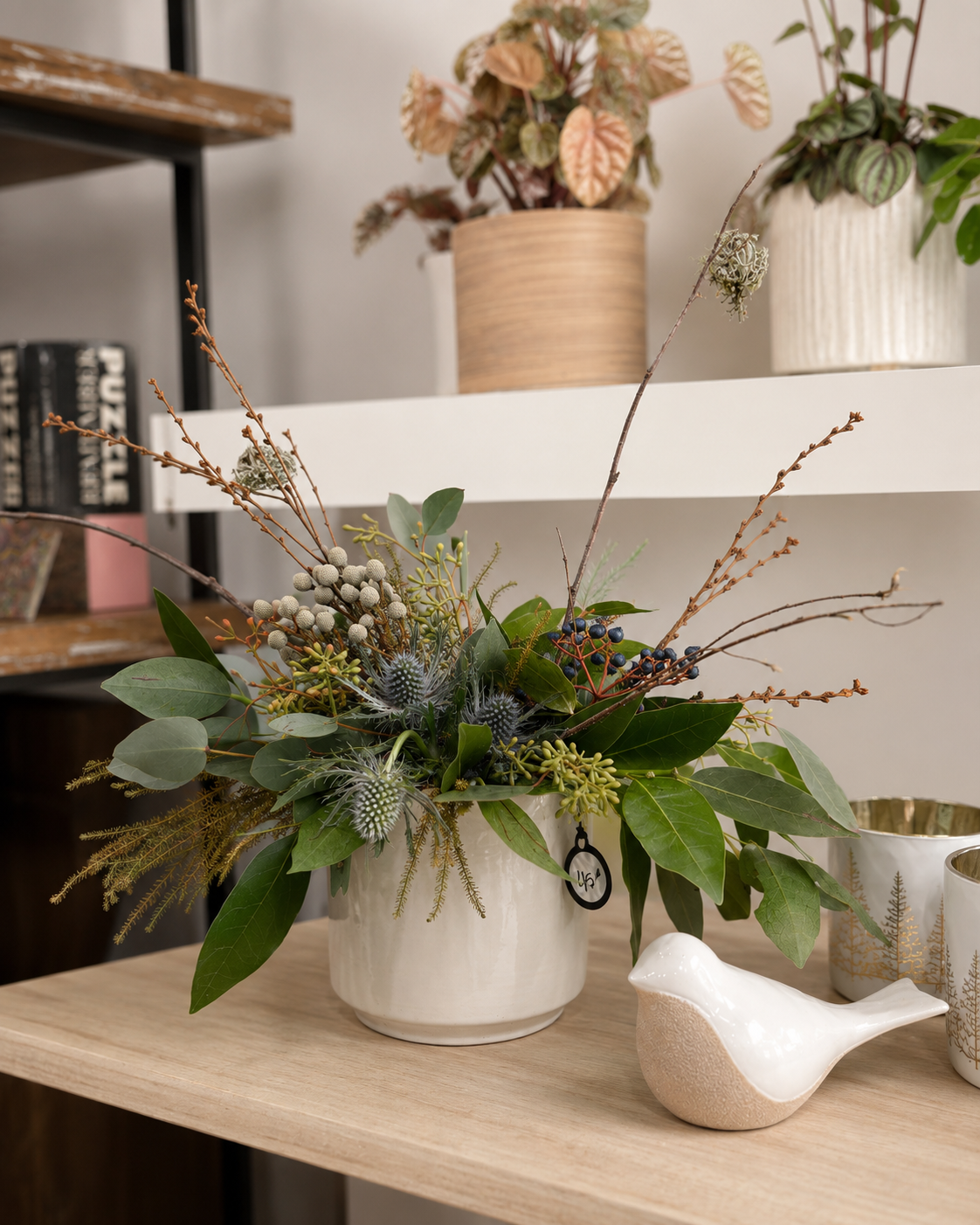Vase blanc contenant un arrangement floral séché sur une étagère à côté d'une petite figurine d'oiseau blanc