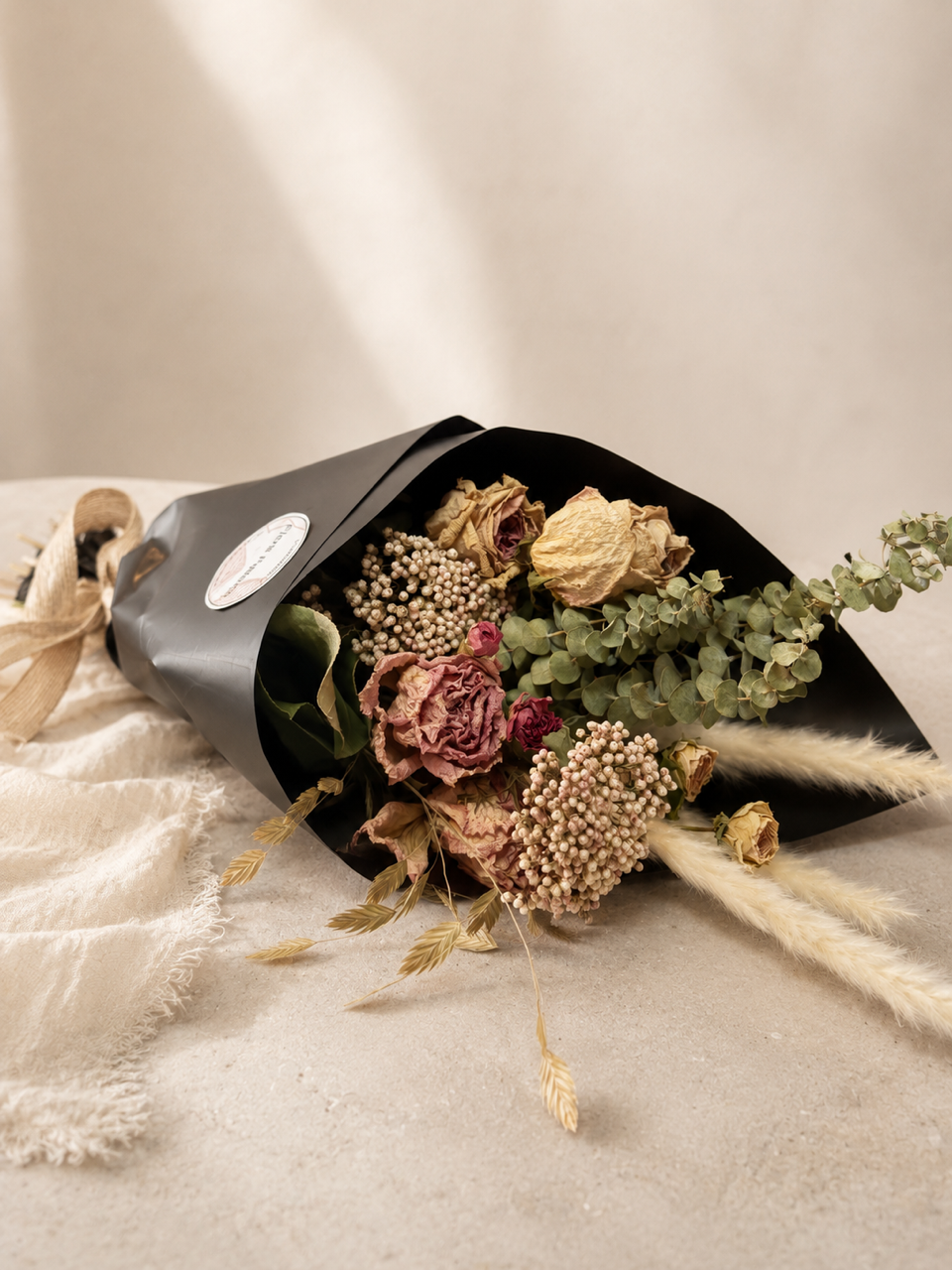 Bouquet de fleurs séchées enveloppé dans du papier noir sur un fond de tissu beige clair