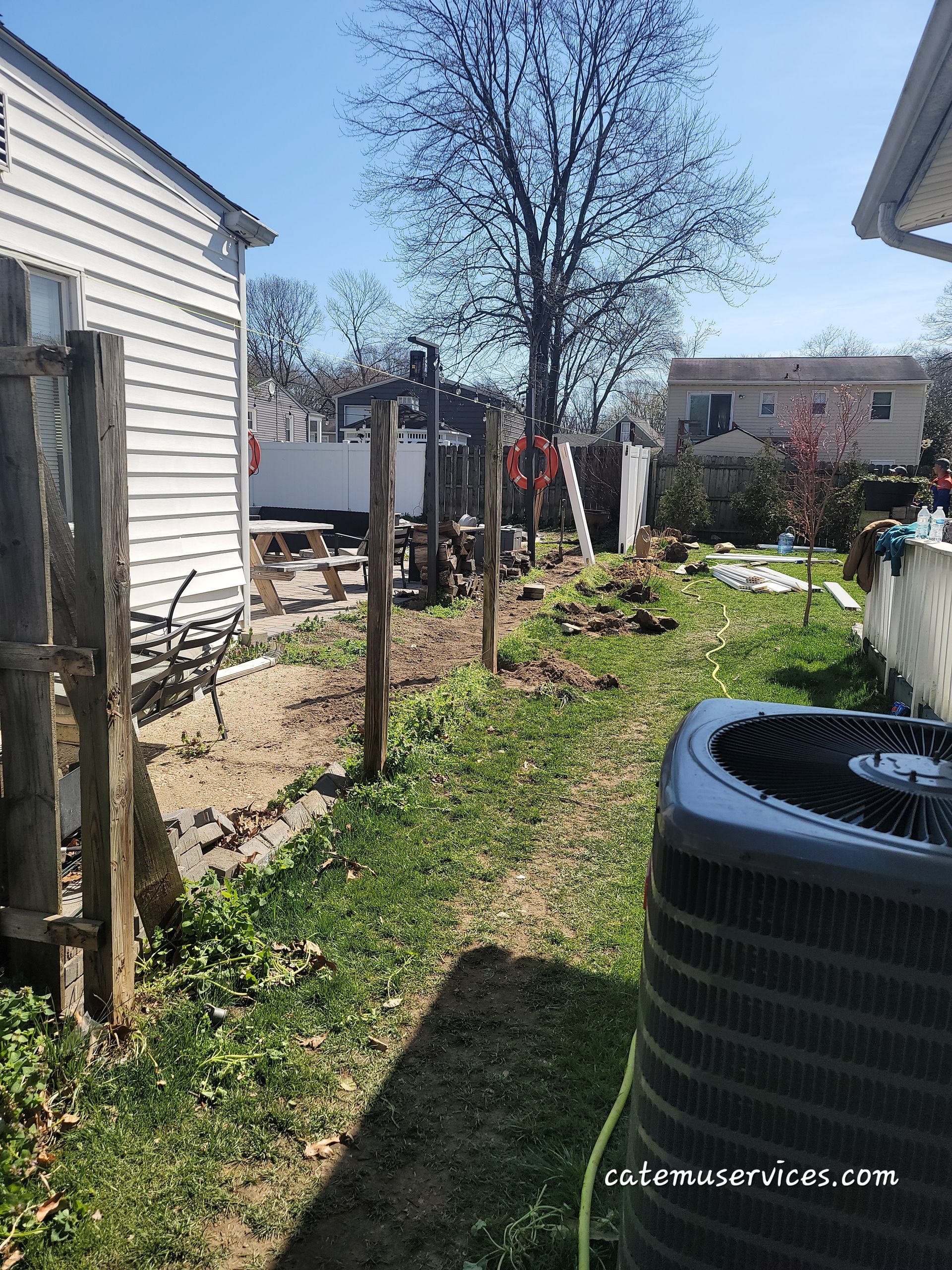 Backyard with fence posts, HVAC unit, small house, and grass under a blue sky.