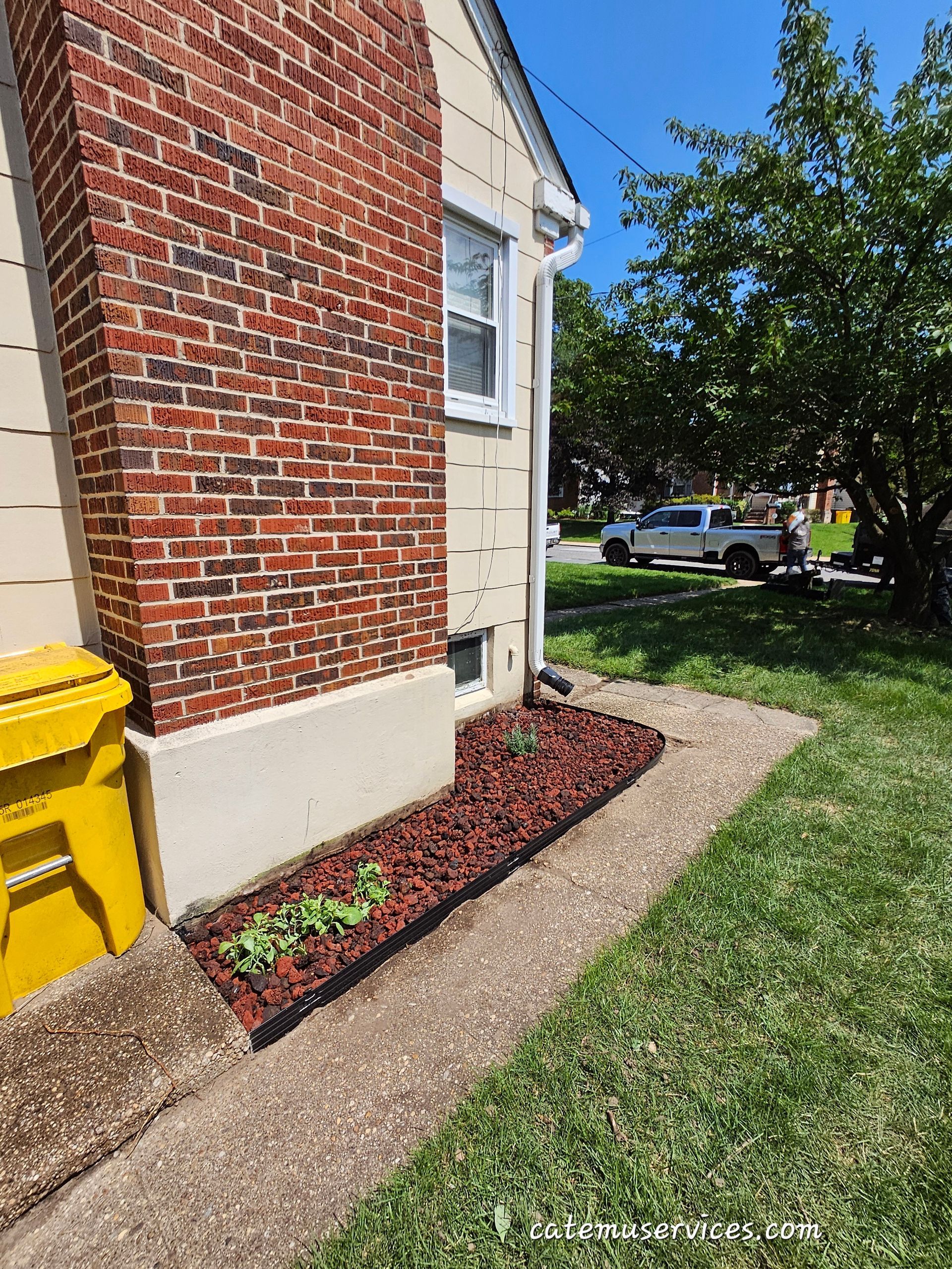 Red brick chimney next to a house with small landscaped bed, sidewalk, and grass.