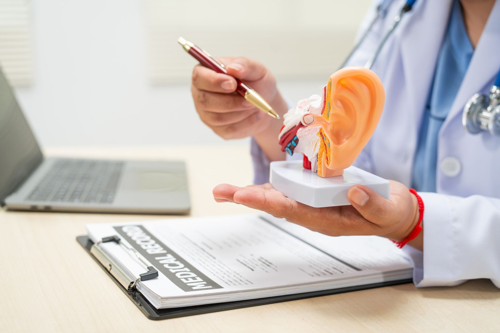 Doctor demonstrating ear anatomy on clipboard beside laptop in a clinical setting