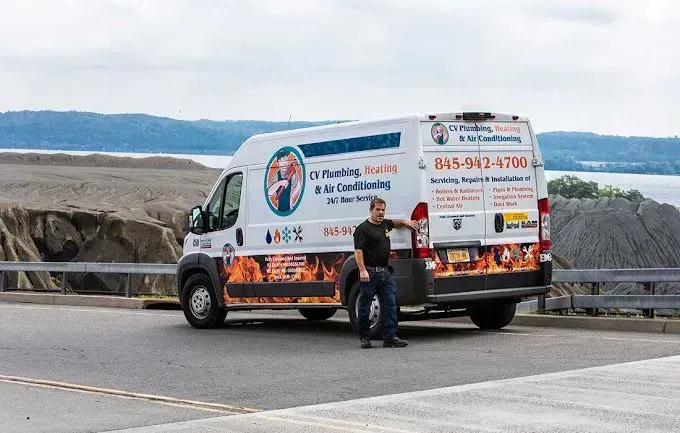 White utility van parked by a rocky waterfront with a person standing beside it
