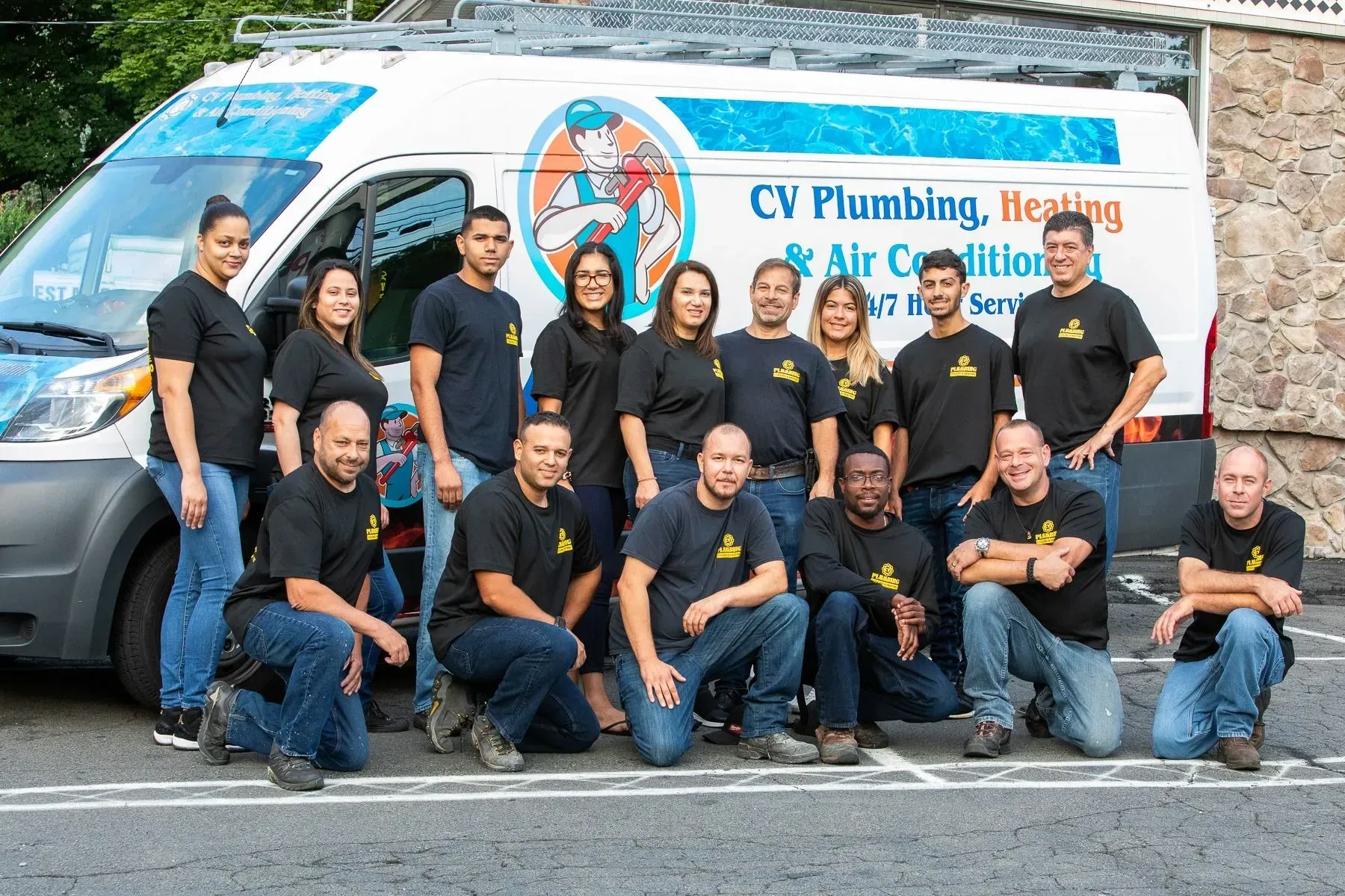 Group of people in black shirts and blue jeans, posing in front of a company van.