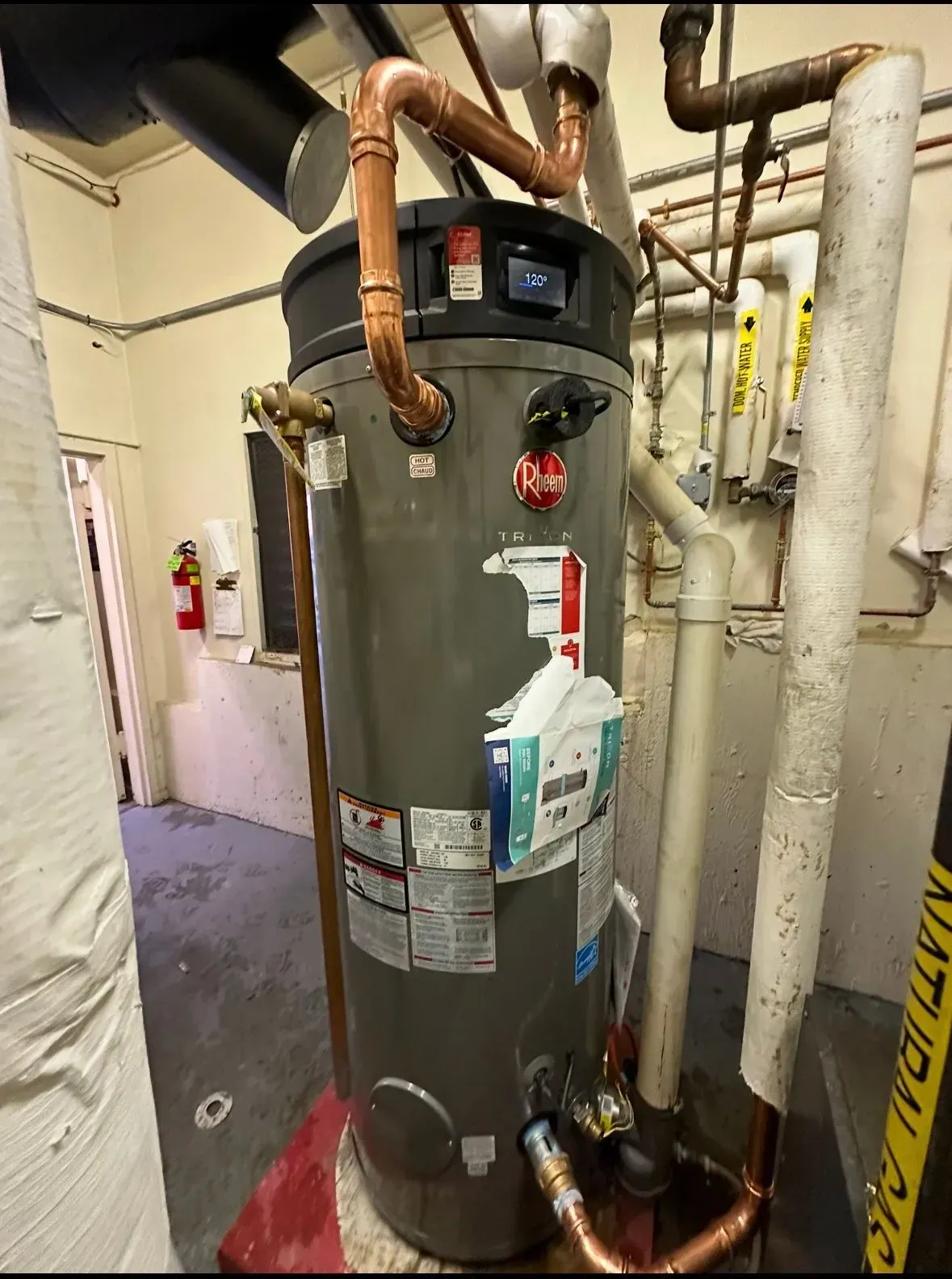 Water heater with copper pipes in an interior room with other pipes and equipment.