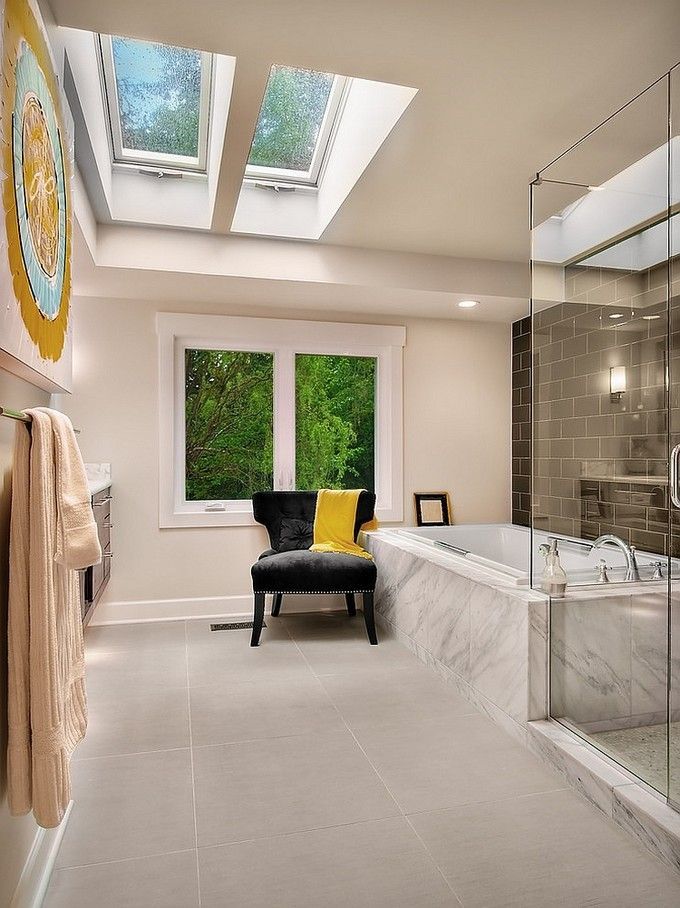 Bathroom with skylights and window overlooking trees, featuring a bathtub and chair with a yellow pillow.