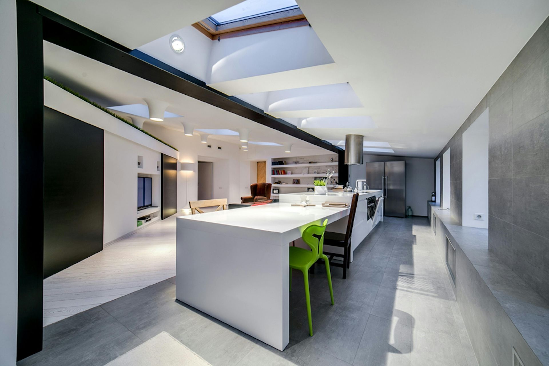 Modern kitchen with white island, green chairs, skylights, and stainless steel appliances.