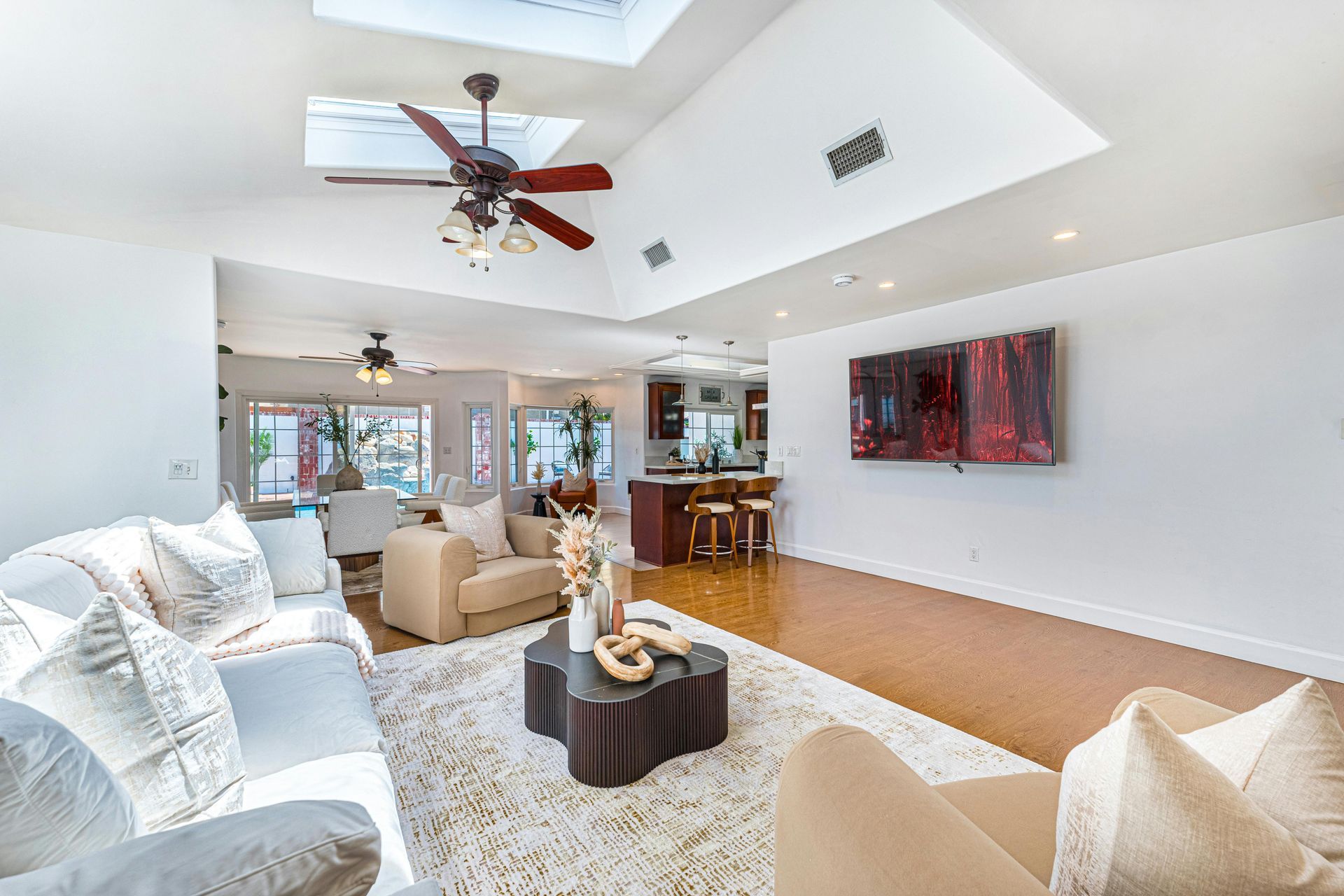 Spacious living room with white walls, skylight, and wood floors. Features sofas, coffee table, and art.