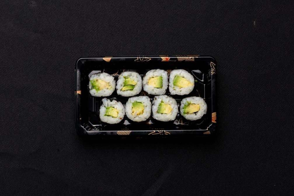 A tray of sushi rolls with avocado on a black background.