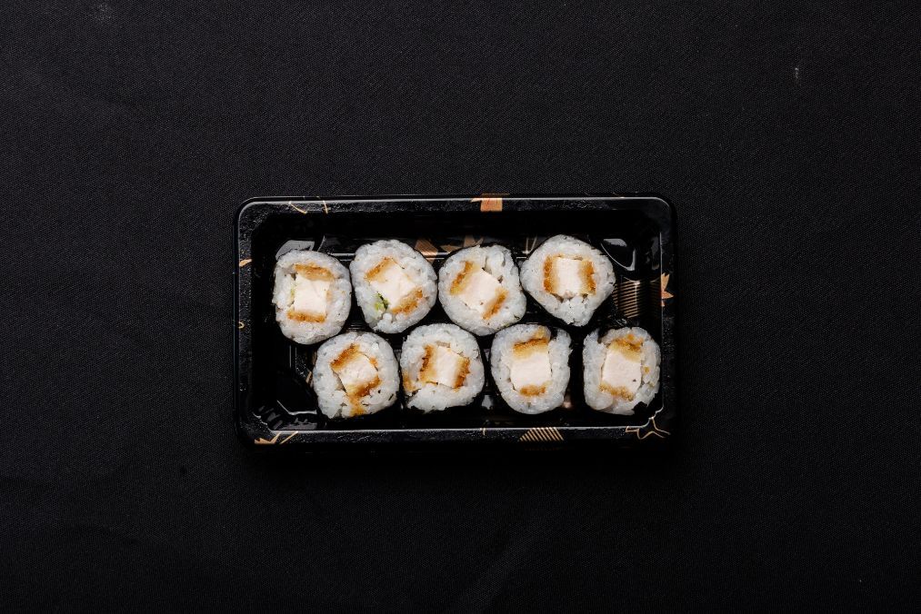 A black tray filled with sushi rolls on a black surface.