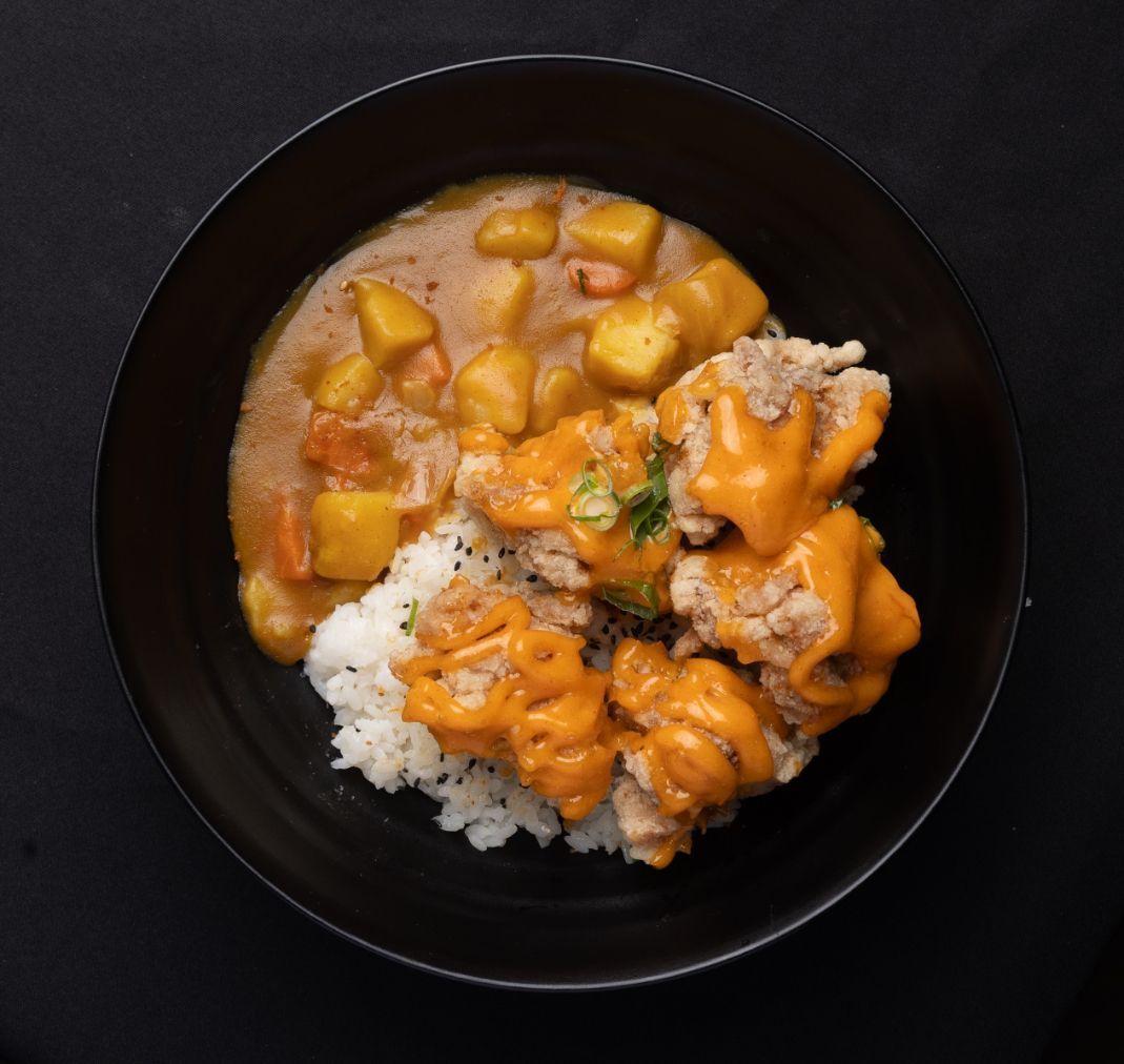 A bowl of food with rice and sauce on a table.
