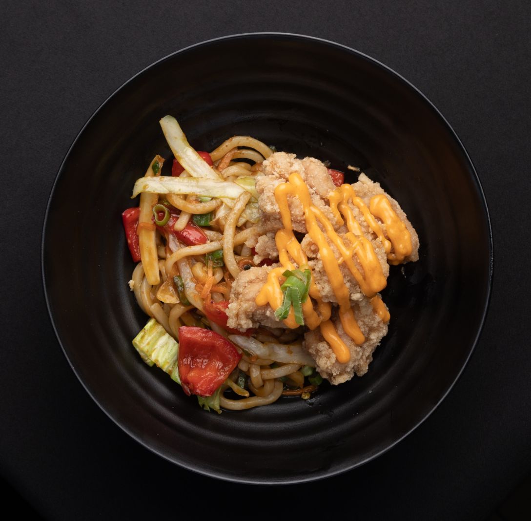 A black bowl filled with noodles chicken and vegetables
