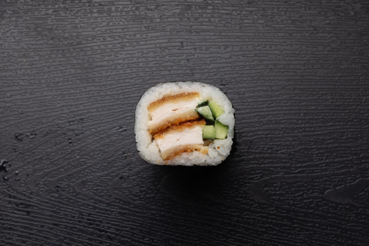 A sushi roll with chicken and cucumber on a black surface.