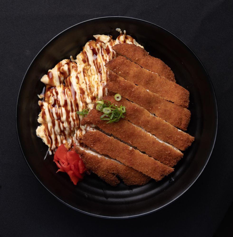 A black plate topped with fried food and sauce on a table.