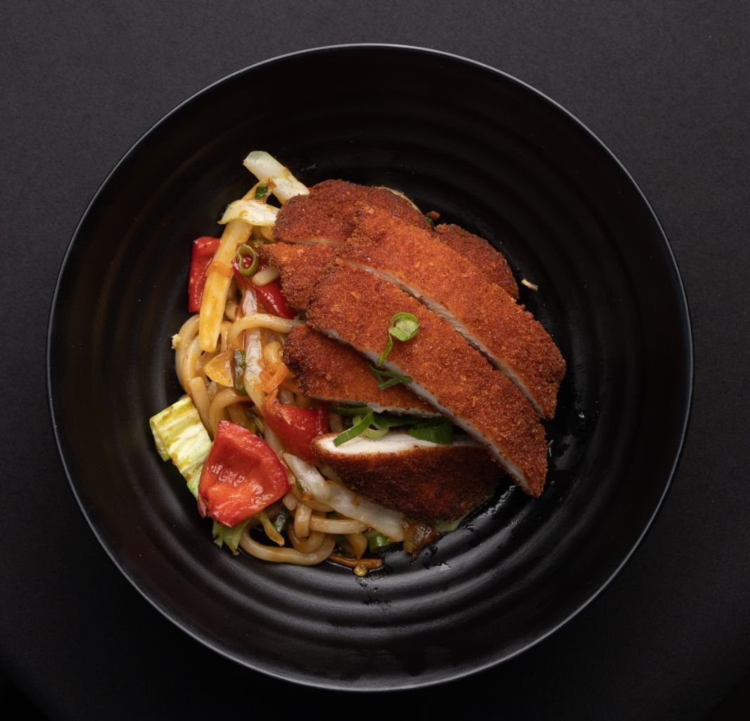 A black bowl filled with meat and vegetables on a table.