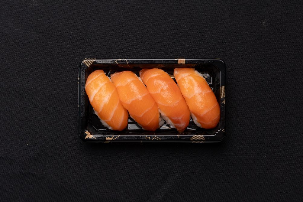 A tray of salmon sushi on a black surface.