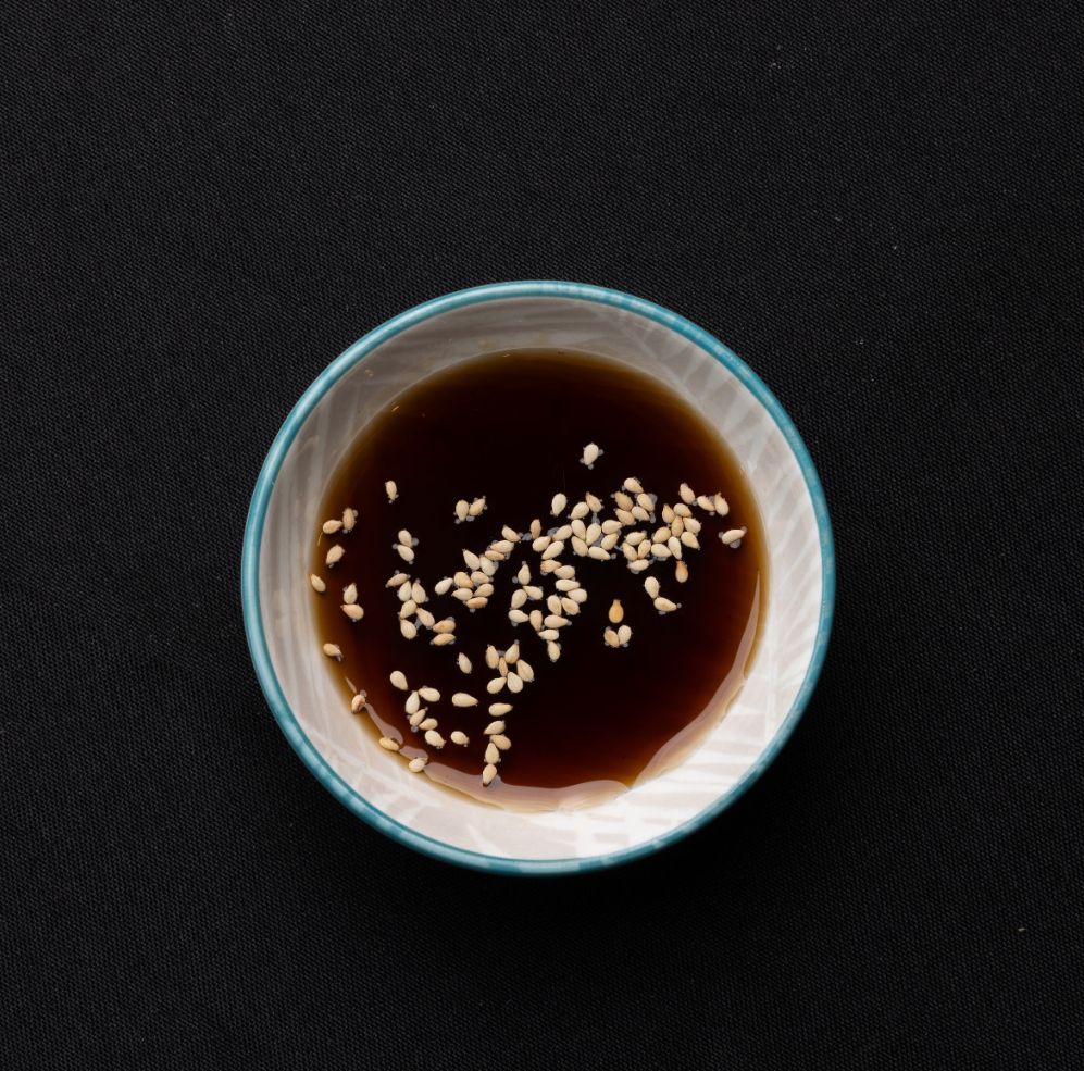 A small bowl of sauce with sesame seeds in it