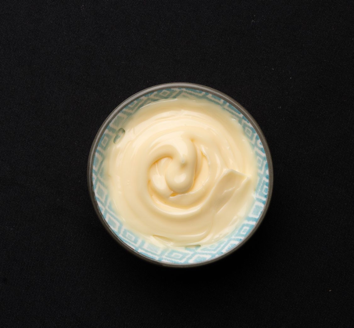 A small bowl of mayonnaise on a black background.