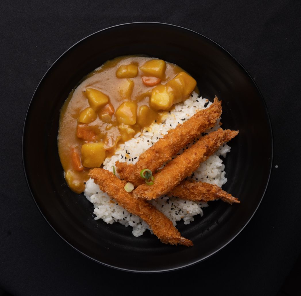 A bowl of food with rice and fried chicken on a table.