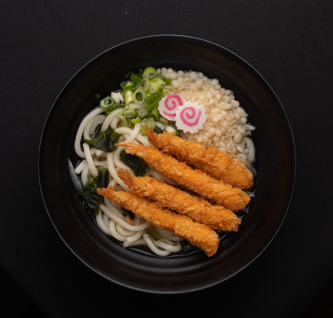 A black bowl filled with noodles , rice and fried shrimp.