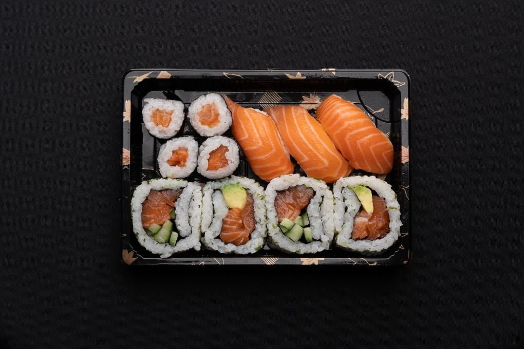 A plastic container filled with sushi and rolls on a black background.