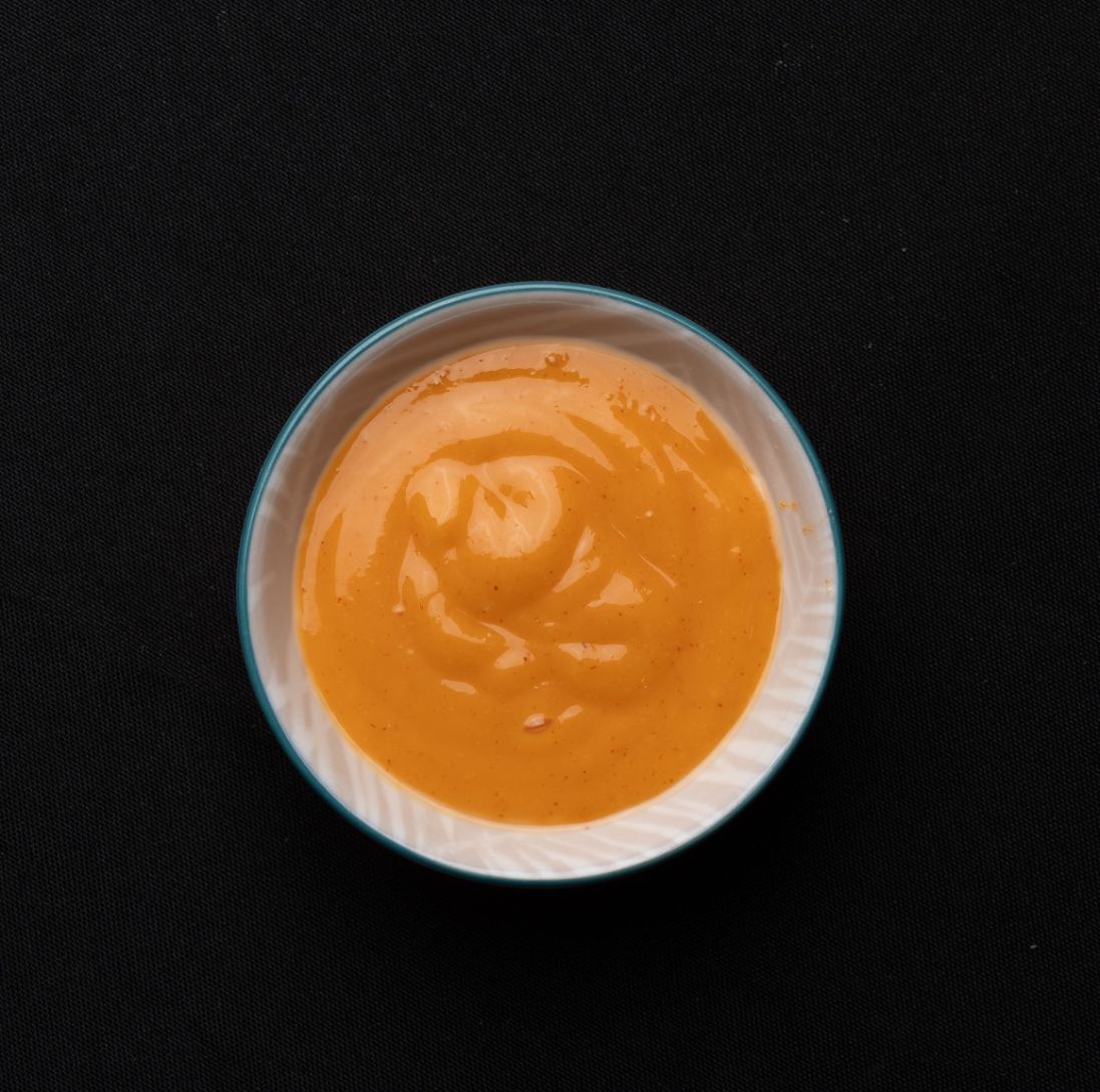 A small bowl of orange sauce on a black surface.