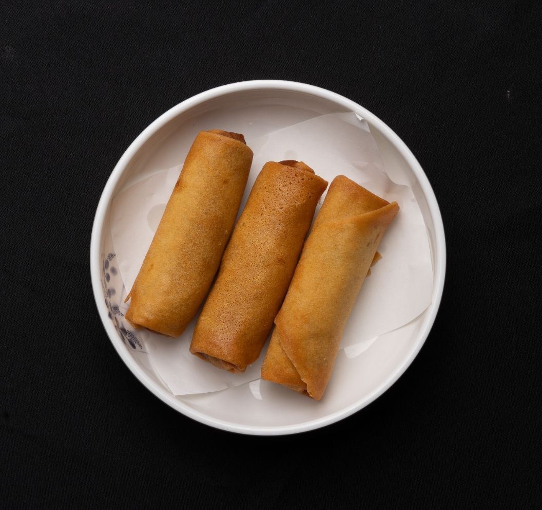 Three egg rolls on a white plate on a black background