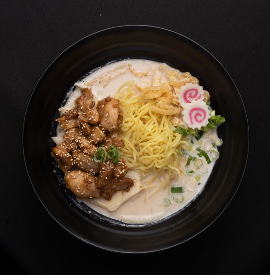 A black bowl filled with noodles and meat on a table.