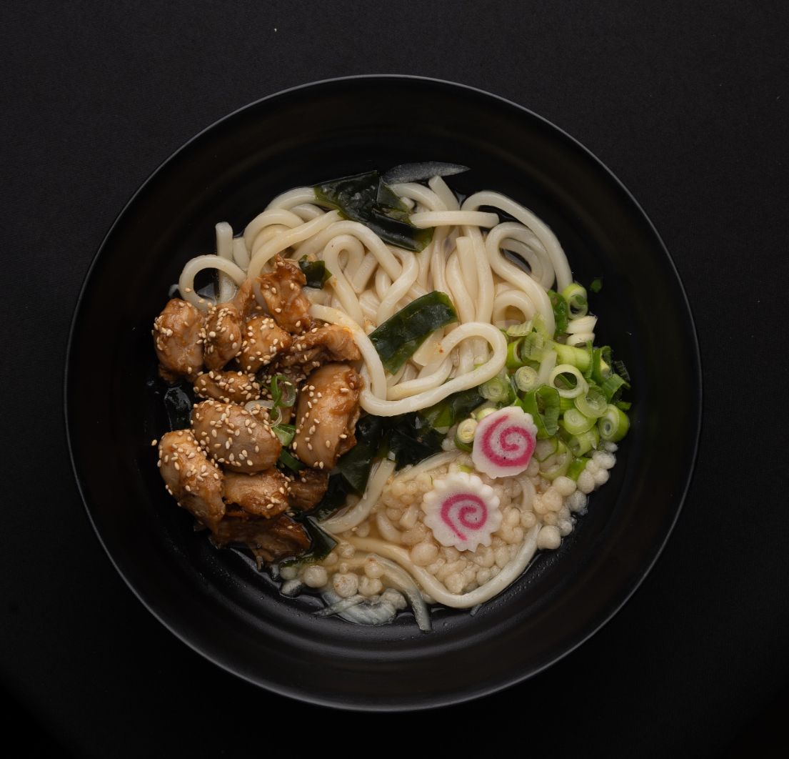 A bowl of noodles with chicken and vegetables on a table.