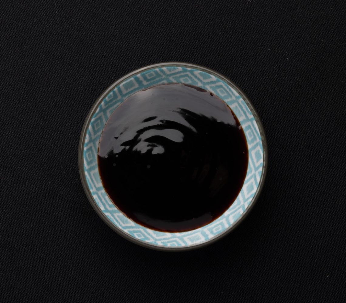 A small bowl of soy sauce on a black background.