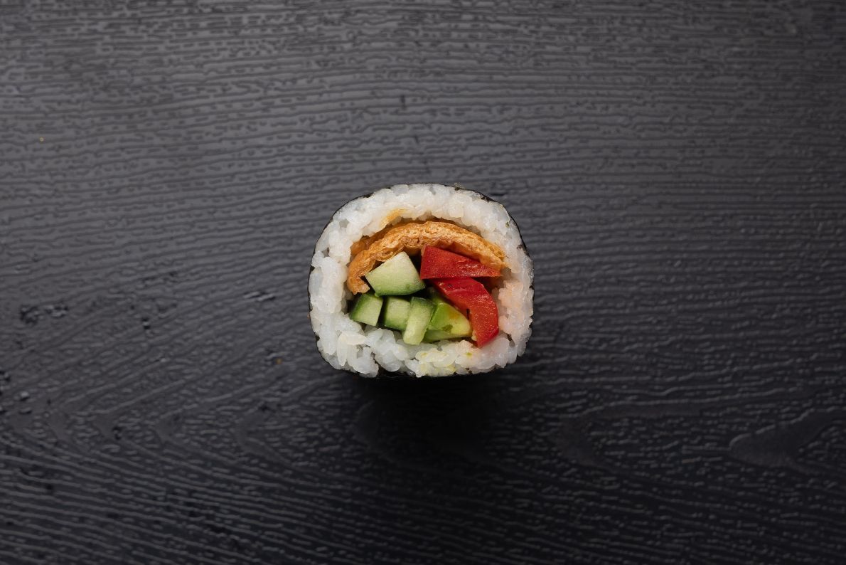 A close up of a sushi roll with vegetables on a black surface.