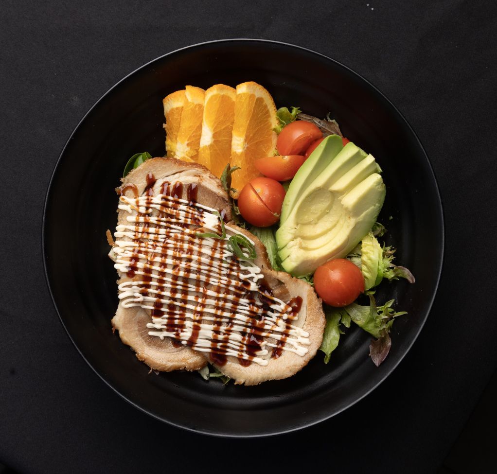 A black plate topped with meat avocado tomatoes and oranges