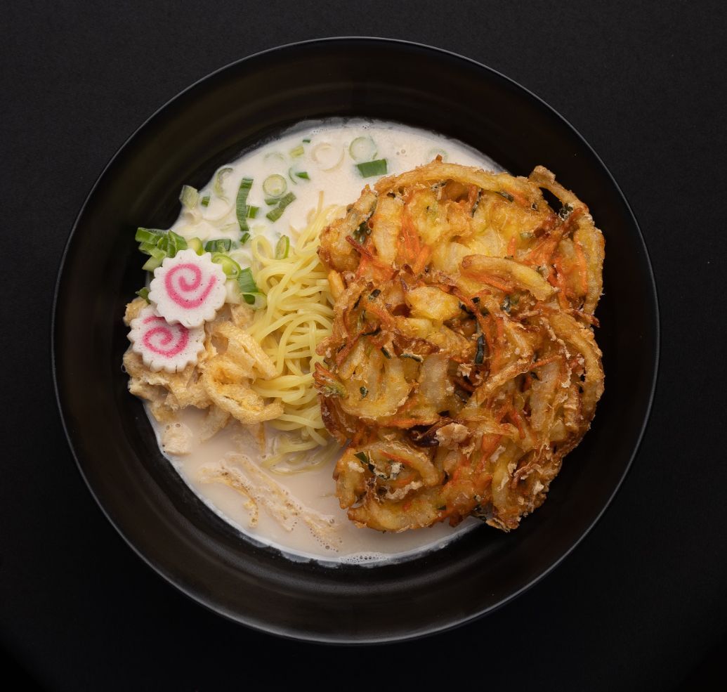 A black bowl filled with noodles and fried food on a table.
