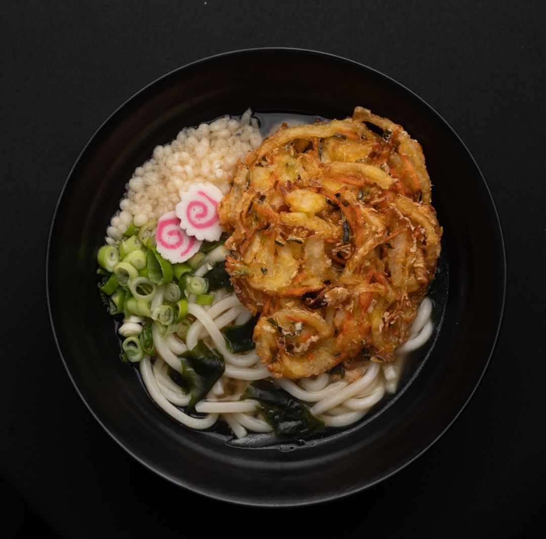 A black bowl filled with noodles and vegetables on a table.