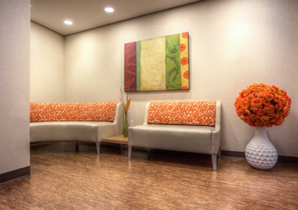 A waiting room with two couches , a vase of flowers and a painting on the wall.