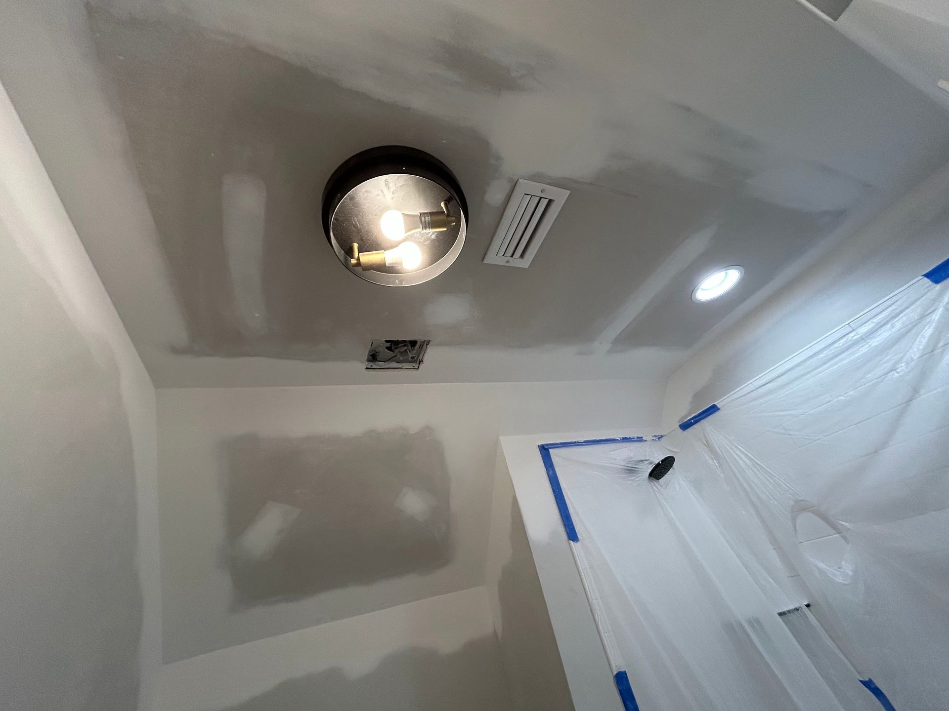 Bathroom ceiling with recessed light, vents, and taped plastic sheeting over a doorway or shower area.