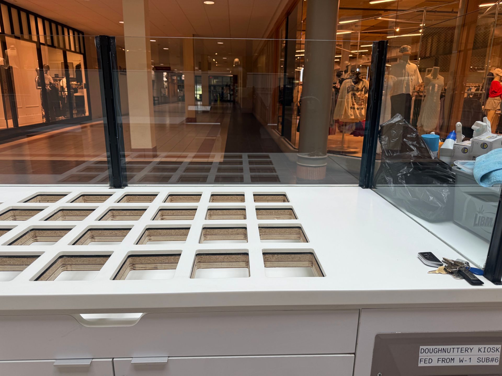 A counter with square openings, protective glass, and a mall hallway in the background.