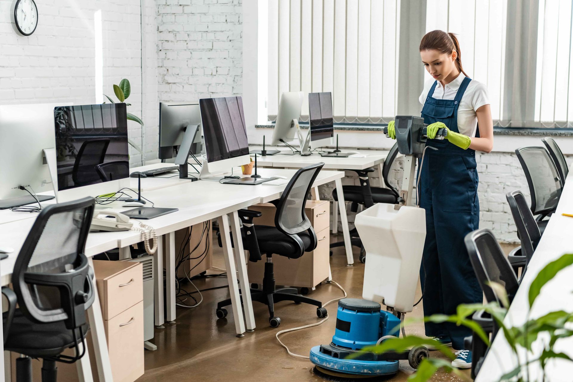 Woman in overalls cleaning an office with a floor machine.