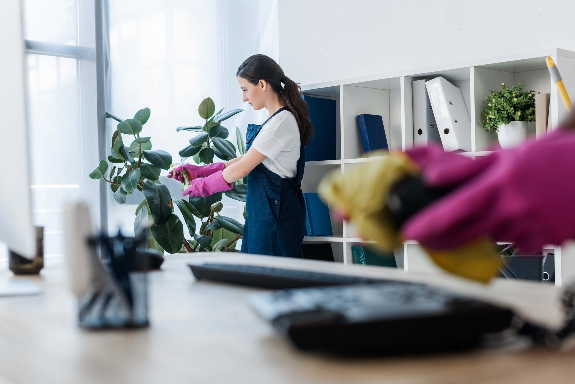 A person wearing pink gloves cleans an office. White shelves are in the background.