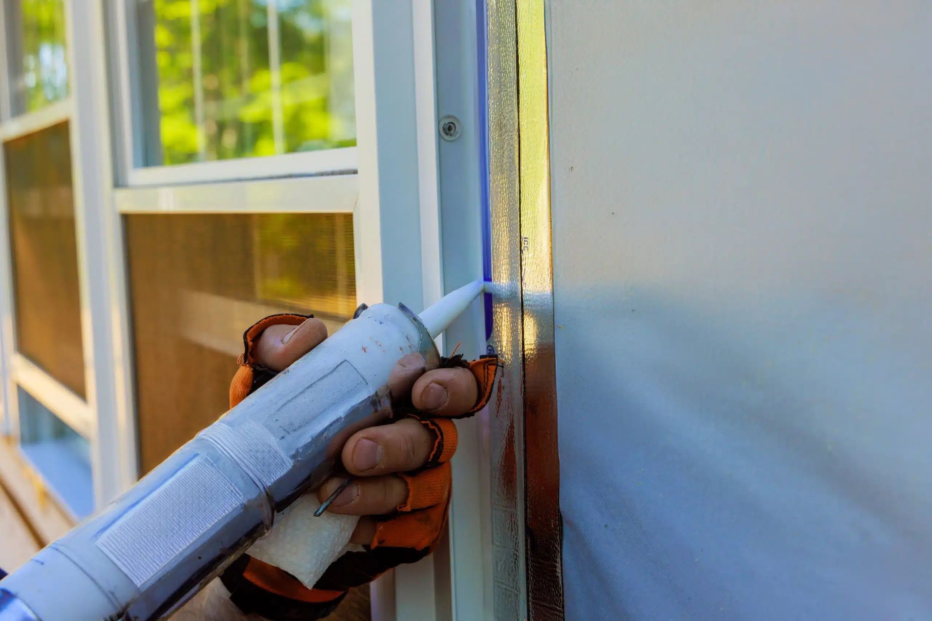 Hand caulking a window frame with a sealant gun, outdoors.