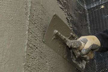 Person using a trowel to apply stucco to a wall with black mesh, close-up.