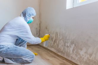 A man in a protective suit is cleaning a wall with a spray bottle.