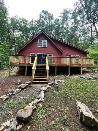 A red house with a large deck in the middle of the woods.