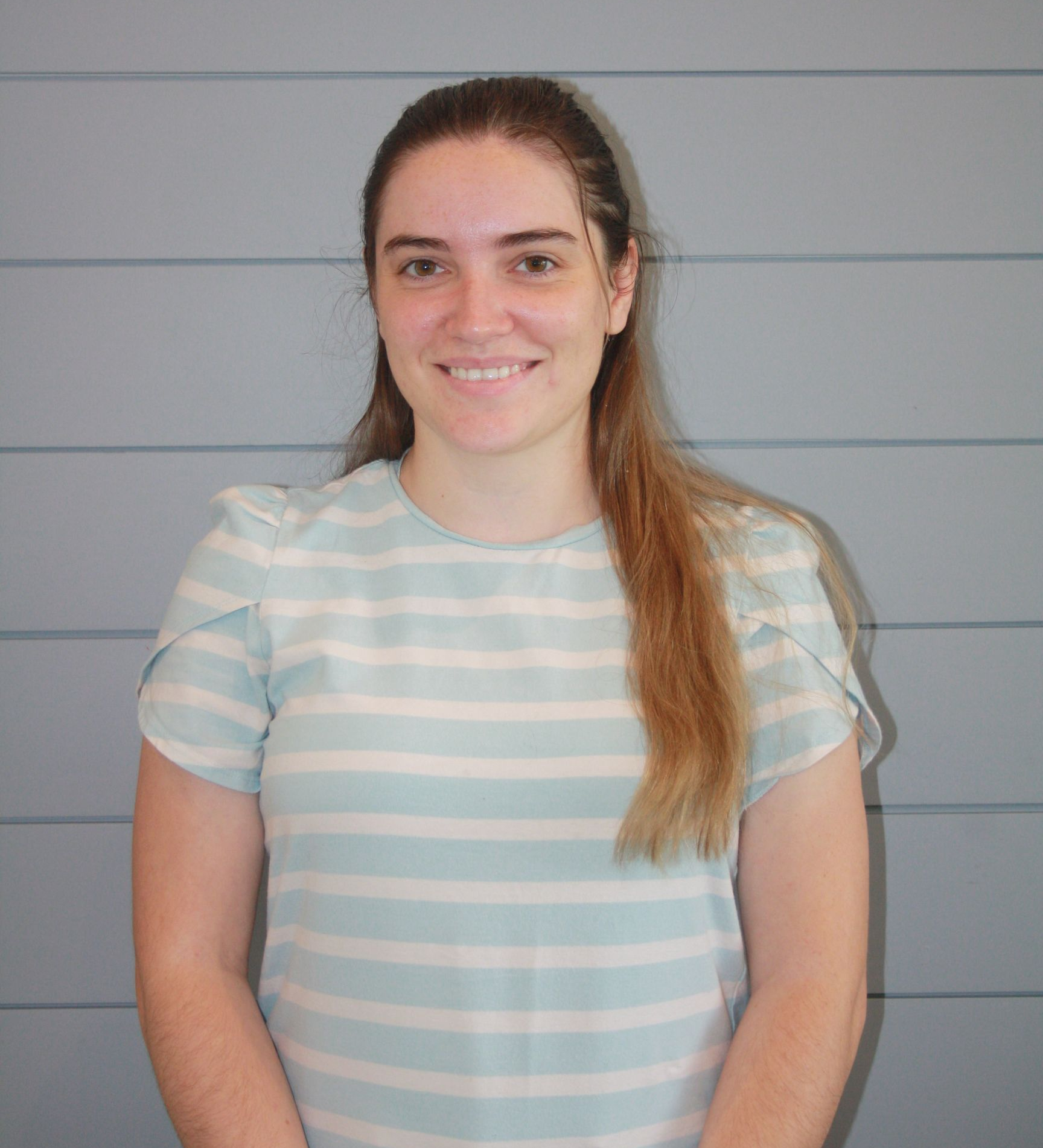 Woman smiling in a light blue striped shirt against a gray wall