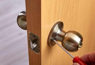 A person is fixing a door knob with a screwdriver.