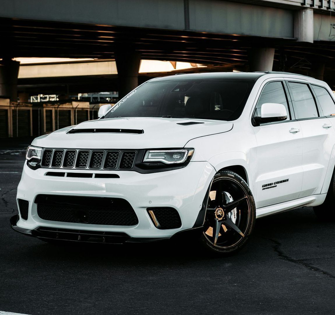 White Jeep Grand Cherokee with custom black wheels, parked under an overpass.